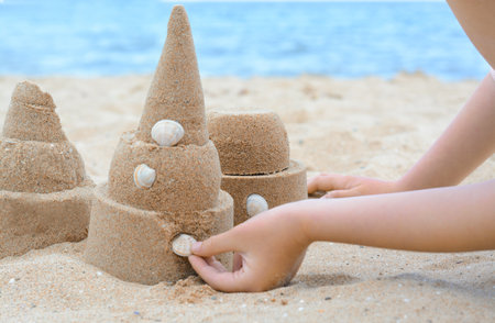 Child decorating sand castle with shell on beach, closeupの写真素材
