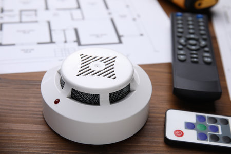 Smoke detector and remote controls on wooden table, closeup. home security system