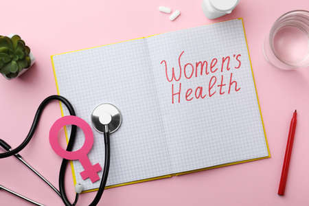Flat lay composition of notebook with words Women Health and female gender sign on pink backgroundの写真素材