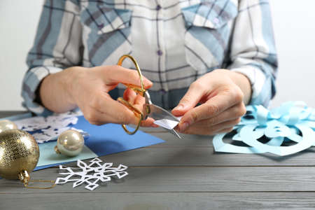 Woman making paper snowflake at gray wooden table, closeupの写真素材