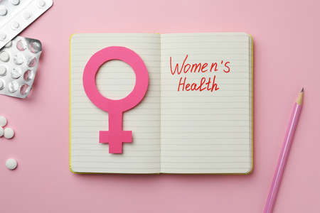 Notebook with female gender sign, pills and text Women's Health on pink background, flat layの写真素材