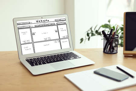 Laptop with sketch of website planning and design on wooden table