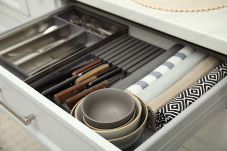 Open drawer of kitchen cabinet with different utensils, dishware and towels, closeupの写真素材