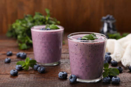Glasses of blueberry smoothie with fresh berries and mint on wooden table, space for textの写真素材
