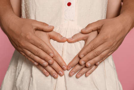 Man hugging his pregnant wife on pink background, closeup