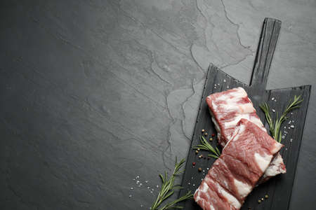 Raw ribs with rosemary and spices on black table, top view. Space for textの写真素材