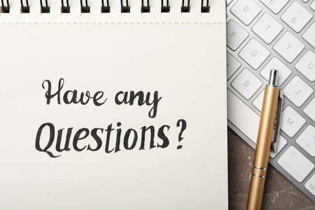 Notebook with phrase HAVE ANY QUESTIONS and keyboard on gray marble table, flat lay