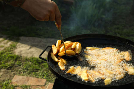 Man cooking delicious potato wedges on frying pan outdoors, closeupの写真素材