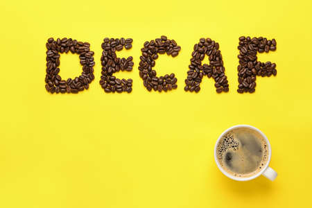 Word Decaf made with coffee beans and cup of hot drink on yellow background, flat lay. Space for textの写真素材