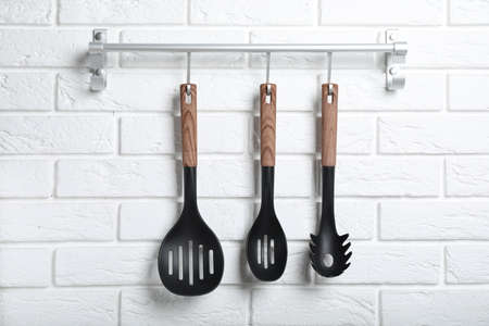 Rack with kitchen utensils hanging on white brick wallの写真素材