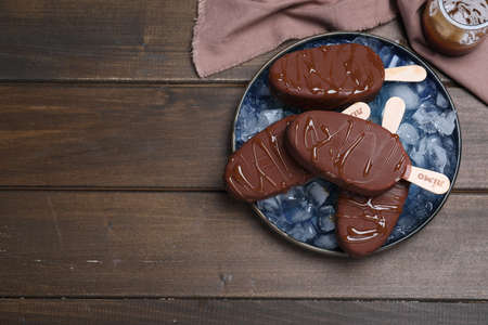 Delicious glazed ice cream bars and ice cubes on wooden table, flat lay. Space for textの写真素材
