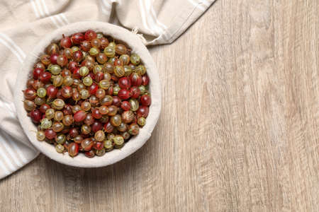 Fresh ripe gooseberries in bowl on wooden table, top view. Space for textの写真素材
