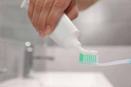 Woman applying toothpaste on brush in bathroom, closeup