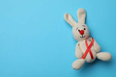 Cute knitted toy bunny with red ribbon on blue background, top view and space for text. AIDS disease awarenessの写真素材