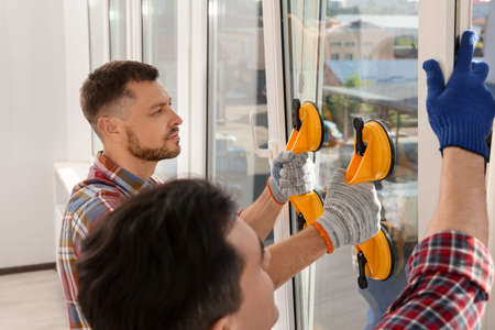 Workers using suction lifters during plastic window installation indoors