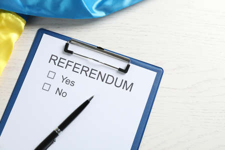 Referendum ballot with pen and flag of Ukraine on white wooden table, flat lay
