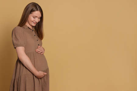 Happy young pregnant woman on light brown background. Space for text