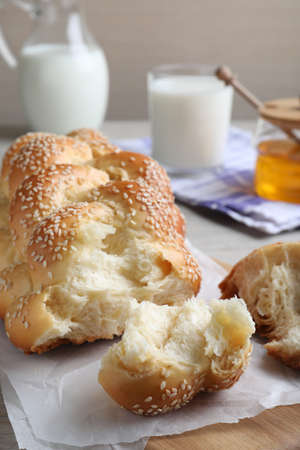 Broken homemade braided bread with sesame seeds on wooden table, closeup. Traditional Shabbat...