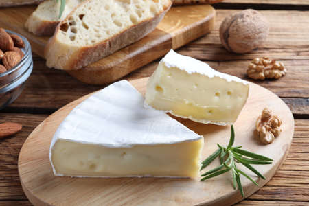 Tasty cut brie cheese with rosemary, bread and nuts on wooden tableの写真素材