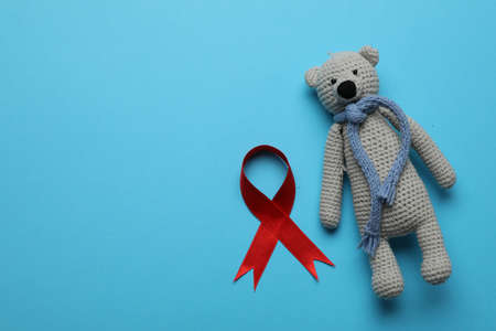 Cute knitted toy bear and red ribbon on blue background, flat lay with space for text. AIDS disease awarenessの写真素材