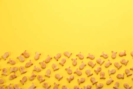 Delicious goldfish crackers on yellow background, flat lay. Space for text