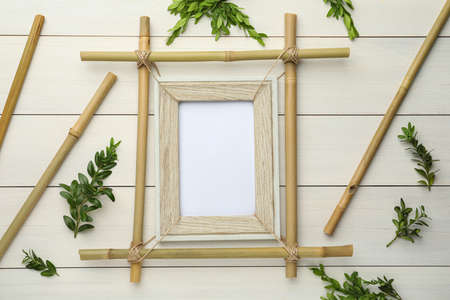 Flat lay composition with bamboo frame and green leaves on white wooden tableの写真素材