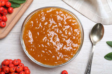 Flat lay composition with delicious rowan jam on white wooden table