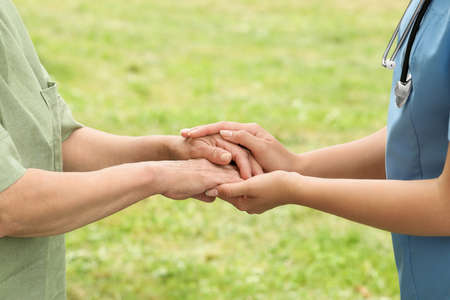 Elderly woman and female caregiver holding hands outdoors, closeupの写真素材
