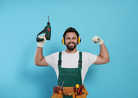 Young worker in uniform with power drill on light blue background