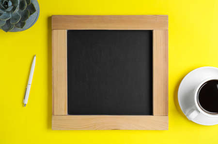 Clean small chalkboard, coffee, pen and plant on yellow background, flat layの写真素材