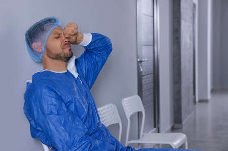 Exhausted doctor sitting on chair in hospital corridor, space for text