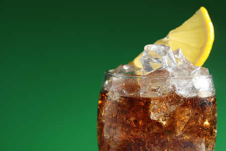 Glass of refreshing soda drink with ice cubes and lemon on green background, closeup. Space for textの写真素材