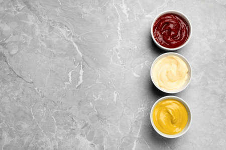 Bowls with mustard, ketchup and mayonnaise on light gray table, flat lay. Space for textの写真素材