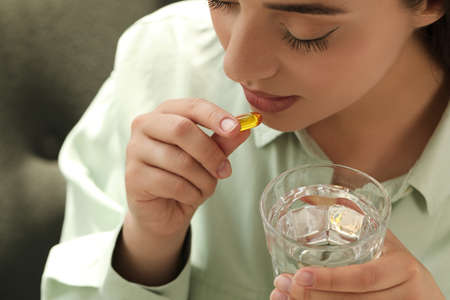 Young woman with glass of water taking dietary supplement pill, closeupの写真素材