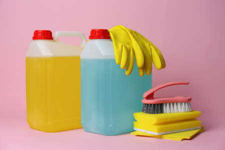 Canisters of cleaning supplies and tools on pink background