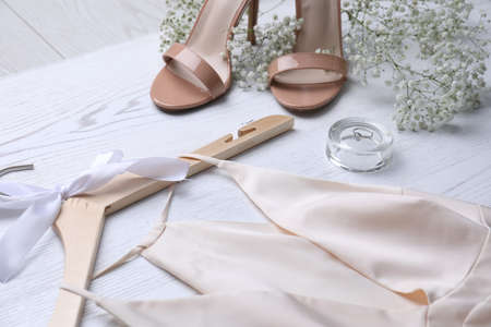 Beautiful wedding dress, shoes, engagement ring and flowers on white wooden background, closeup