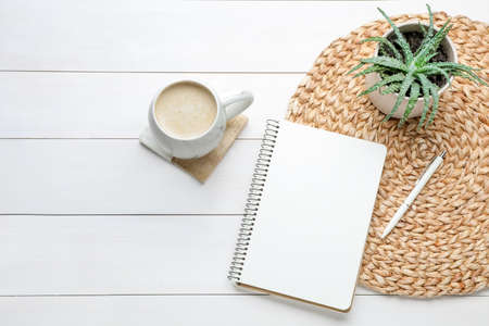 Mug of coffee with stylish cup coaster, houseplant and notebook on white wooden table, flat lay. Space for textの写真素材