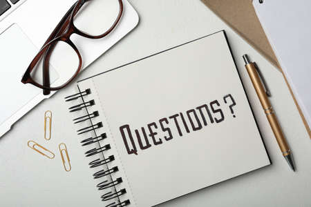 Notebook with word QUESTIONS, laptop and pen on white table, flat layの写真素材