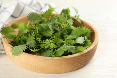Wooden plate with fresh stinging nettle leaves on white table, closeupの写真素材