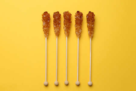 Wooden sticks with sugar crystals on yellow background, flat lay. Tasty rock candiesの写真素材