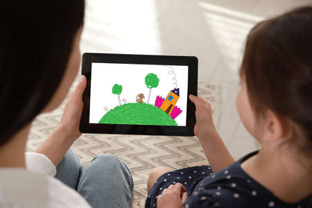 Little girl showing her mother tablet with cute drawing at home. child art