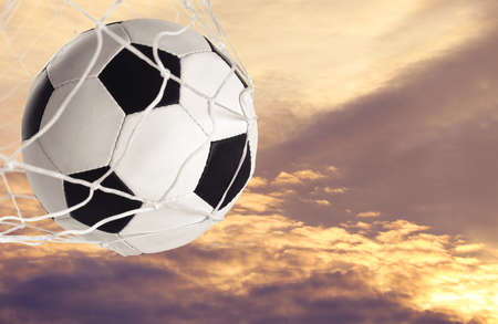 Soccer ball in net against sky at sunsetの写真素材