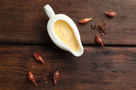 Tasty sauce in gravy boat, small onion bulbs and spice on wooden table, flat layの写真素材
