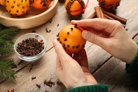 Woman decorating fresh tangerine with cloves on wooden table, closeup. Making Christmas pomander ballsの写真素材