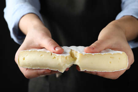 Woman breaking delicious brie cheese on black background, closeup