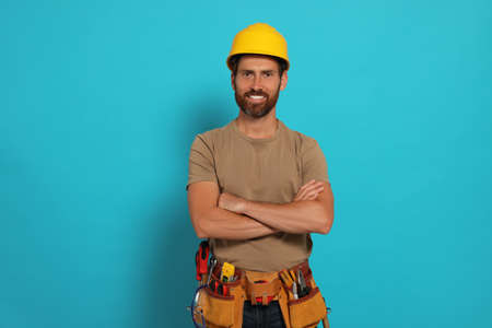 Professional builder in hard hat with tool belt on light blue backgroundの写真素材