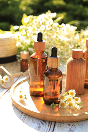 Bottles of essential oil and flowers on white wooden table outdoorsの写真素材