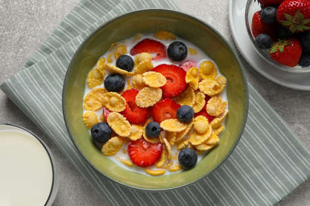 Corn flakes with berries in bowl served on gray table, flat lay