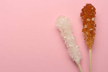 Wooden sticks with sugar crystals and space for text on pink background, flat lay. Tasty rock...