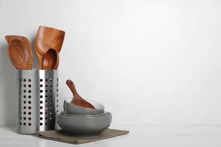 Set of wooden kitchen utensils and bowls on white table. Space for text